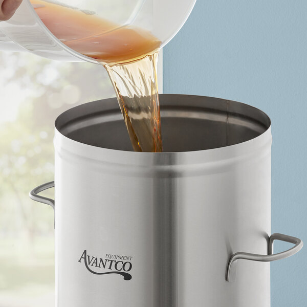A person pouring brown liquid into a stainless steel Avantco iced tea dispenser.