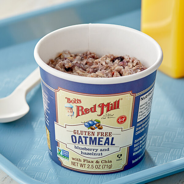 A white bowl of Bob's Red Mill Blueberry Hazelnut oatmeal on a tray with a spoon.
