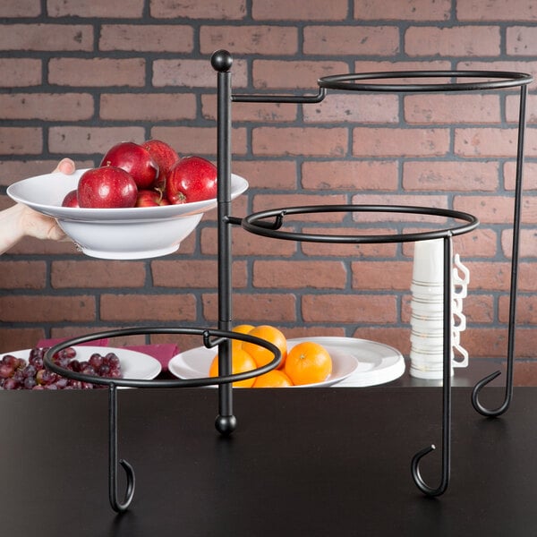 An American Metalcraft Ironworks three-tier round display stand holding a bowl of apples on a table.