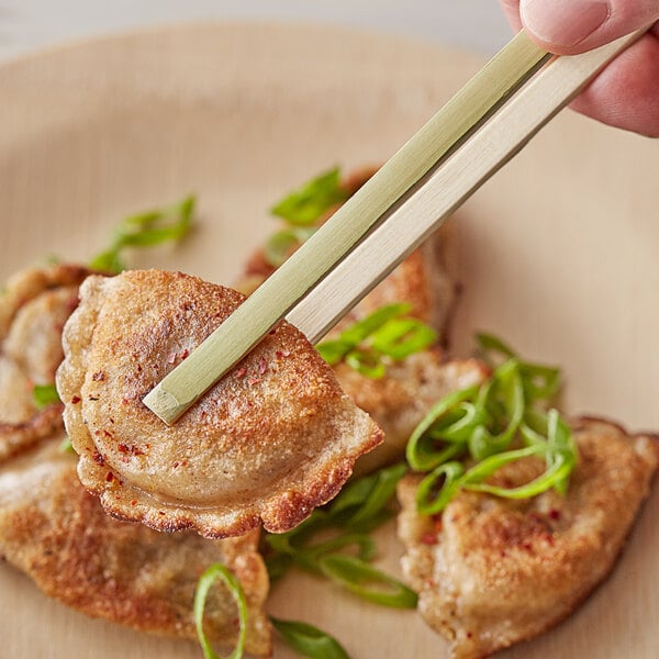 A person using EcoChoice bamboo tongs to pick up food from a plate.