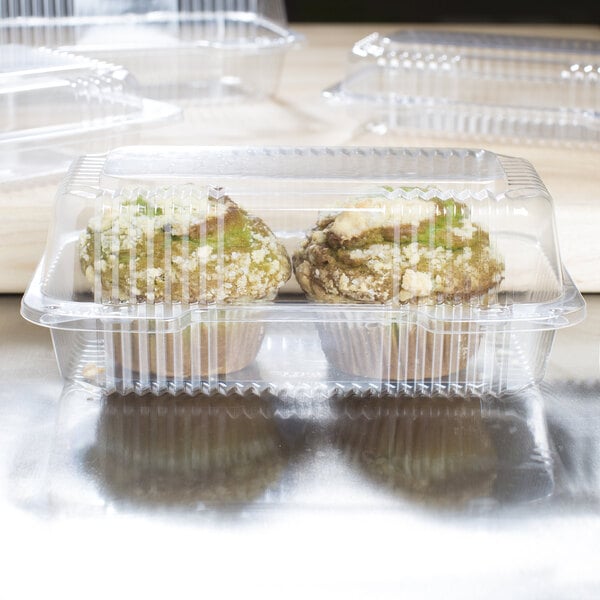 Clear plastic Dart containers holding two muffins on a table.
