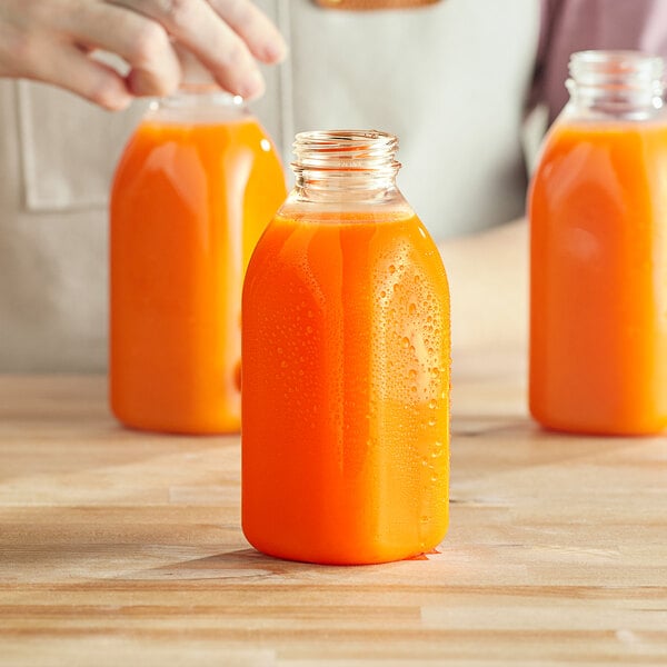 A hand pouring orange juice from a Milkman square PET juice bottle into a glass.