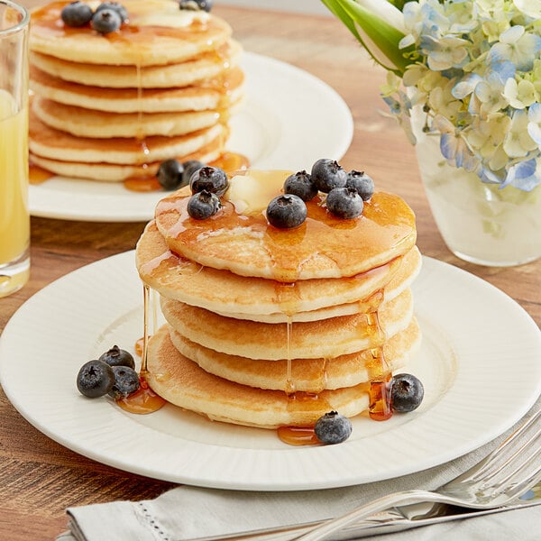 A stack of pancakes with syrup and blueberries on a white plate.