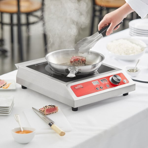 A person cooking a piece of meat on an Avantco countertop induction range.