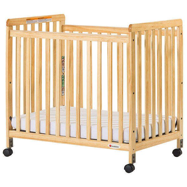 A Foundations SafetyCraft natural wood crib with a mattress on it.