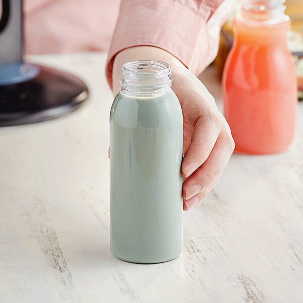 A hand holding an 8 oz. clear round PET juice bottle.