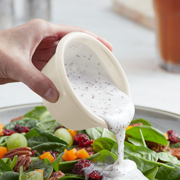 A hand pouring white dressing into a bowl of salad using a white Acopa ramekin.