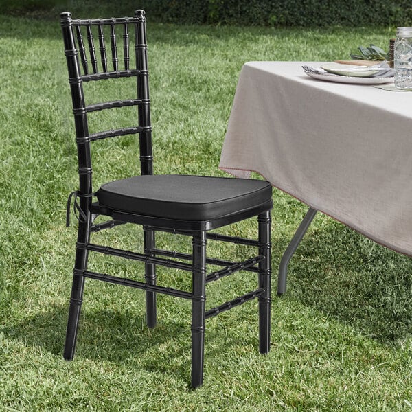 A black Lancaster Table & Seating Chiavari chair with a black cushion on a table in the grass.