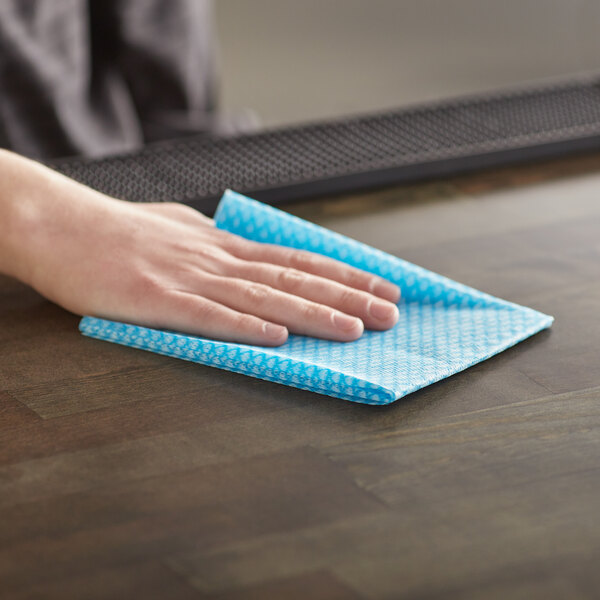 A hand using a Choice blue foodservice wiper to clean a table.