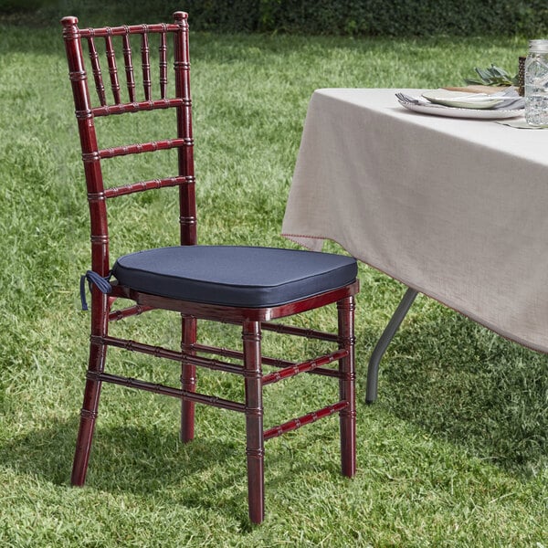 A Lancaster Table & Seating mahogany Chiavari chair with a navy blue cushion next to a table.