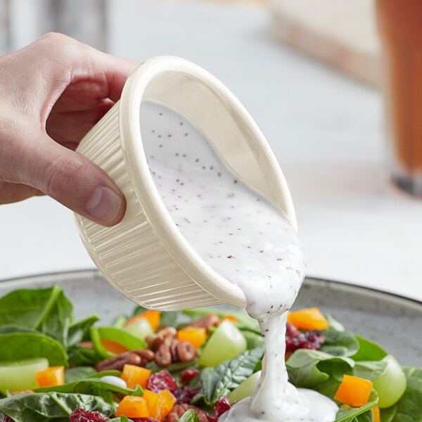 A person using an Acopa Bone White fluted ramekin to pour dressing onto a salad.