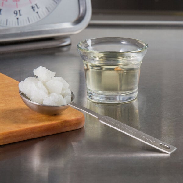 A spoon with white sugar on it next to a bowl of white food and a glass of liquid.