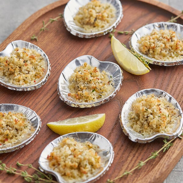 A wooden tray with six small Royal Paper foil clam shells filled with food on a wooden surface.