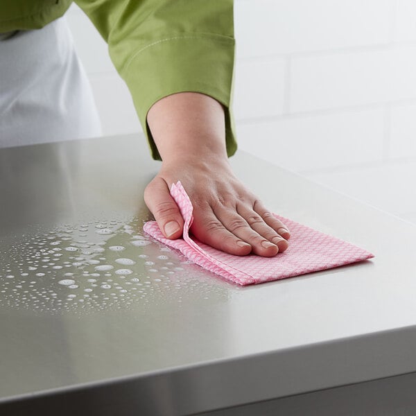 A person using a pink Choice standard duty foodservice wiper to clean a stainless steel countertop.