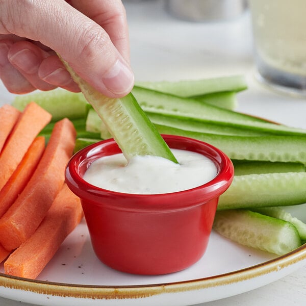 A person using a red Acopa ramekin to dip a carrot into ranch dressing.