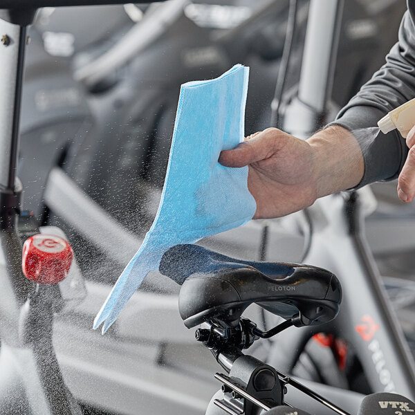A person cleaning a black bicycle seat with a blue Lavex medium-duty wiper.