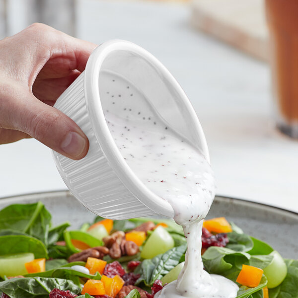 A person using an Acopa white fluted melamine ramekin to pour dressing onto a salad.
