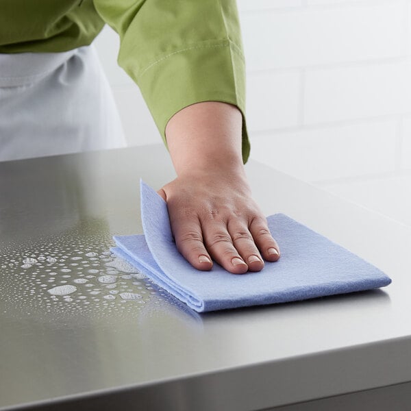 A person using a ChoiceHD blue cloth to clean a stainless steel counter.