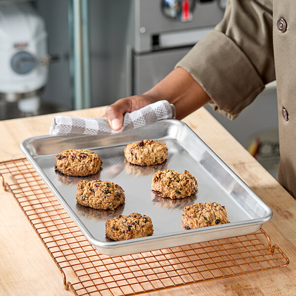 A heavy-duty quarter size aluminum sheet pan with six cookies on it, being held by a person using a towel.