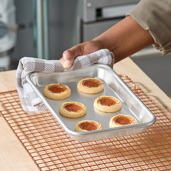 An aluminum eighth size bun or sheet pan with six cookies, being held with a towel.