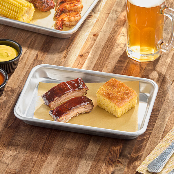 A small rectangular aluminum sheet pan with a wire-reinforced rim, holding two pieces of barbecue ribs and a square of cornbread.