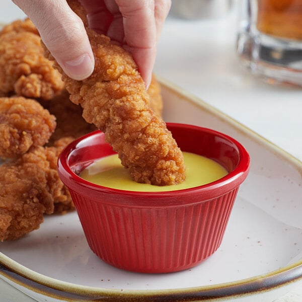 A person dipping a fried chicken piece into a red Acopa fluted ramekin of sauce.
