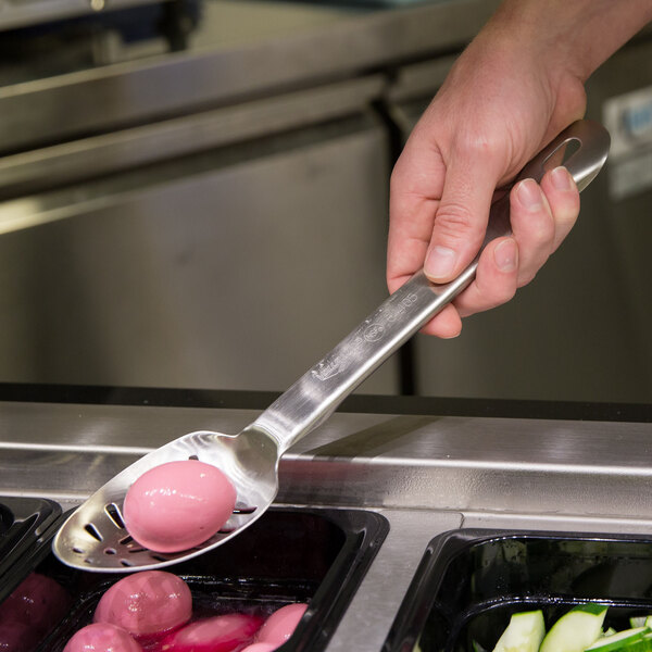 A person using a Vollrath Jacob's Pride slotted stainless spoon to serve food