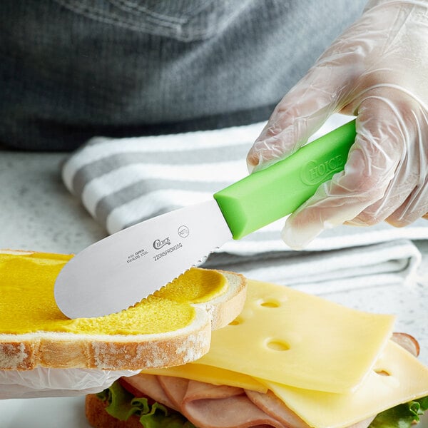 A person using a Choice scalloped sandwich spreader to cut a sandwich.