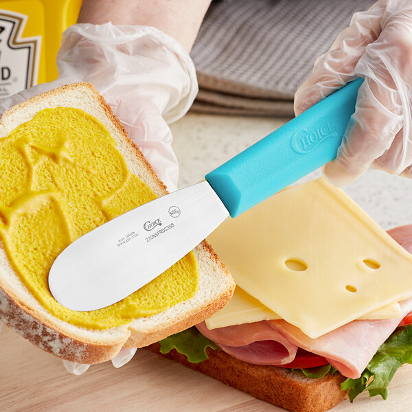 A person using a Choice stainless steel sandwich spreader to spread butter on a piece of bread.