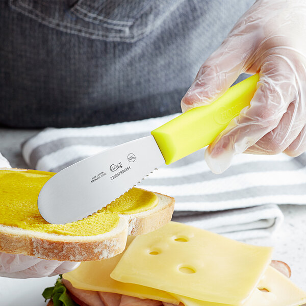 A person spreading butter on a piece of bread with a Choice scalloped sandwich spreader.