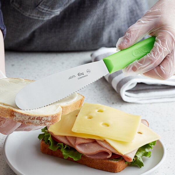 A person spreading a sandwich with a Choice sandwich spreader with a neon green handle.