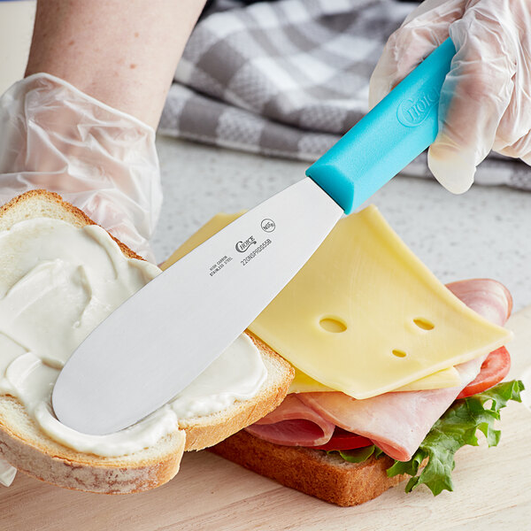 A person using a Choice sandwich spreader with a blue handle to spread butter on a sandwich.