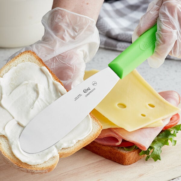 A person using a Choice stainless steel sandwich spreader to spread butter on a sandwich.