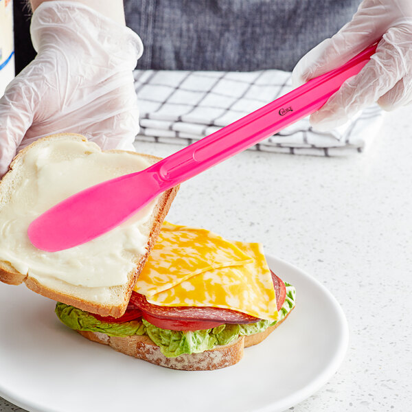 A person holding a Choice pink polypropylene sandwich spreader over a sandwich.