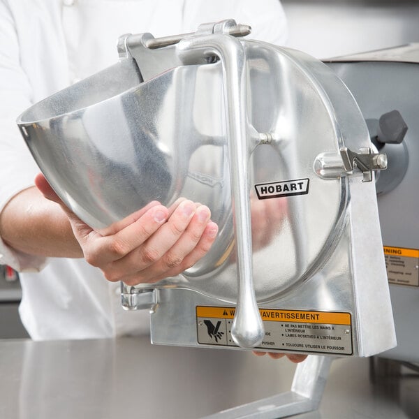 A person holding a Hobart VS9-13 metal slicer attachment.