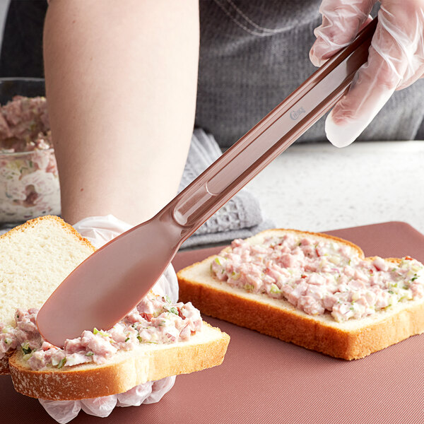 A close-up of a sandwich with a Choice brown-handled sandwich spreader spreading food on a piece of bread.