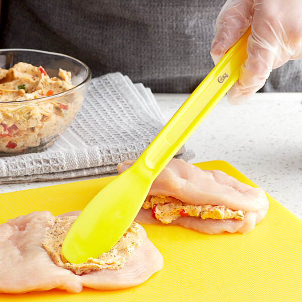 A person using a yellow Choice sandwich spreader to put food on a yellow cutting board.