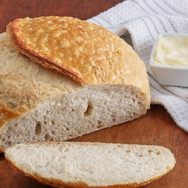 A loaf of bread with a round crust on a wooden surface with a white bowl of butter.