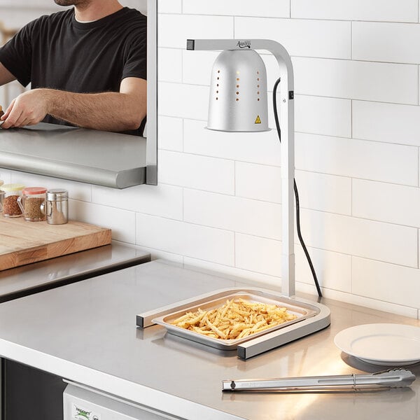 A man in a black shirt using an Avantco countertop heat lamp to cook food on a counter.