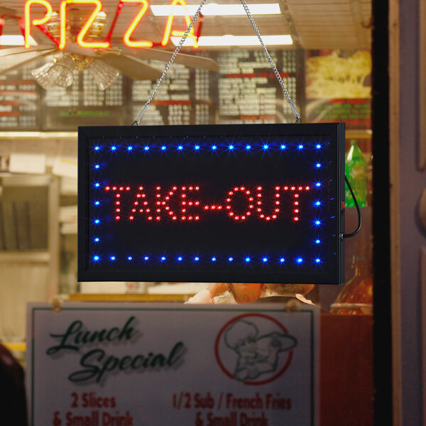 A rectangular LED sign that says "Take Out" on a counter in a pizza parlor.