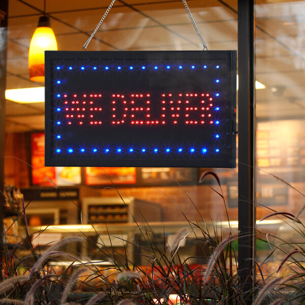 A rectangular LED sign that says "We Deliver" in red and blue lights.