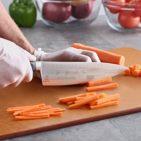 A person cutting carrots on a cutting board with a Mercer Culinary Competition Knife.