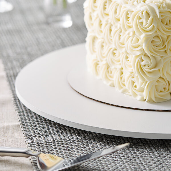 A white cake with frosting on a 22" white circular melamine-coated wood cake board.