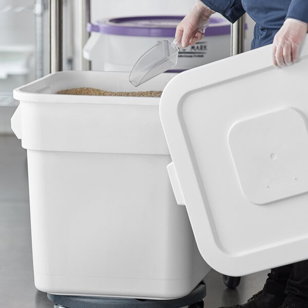 A woman using a plastic scoop to fill a Baker's Mark white ingredient storage bin.