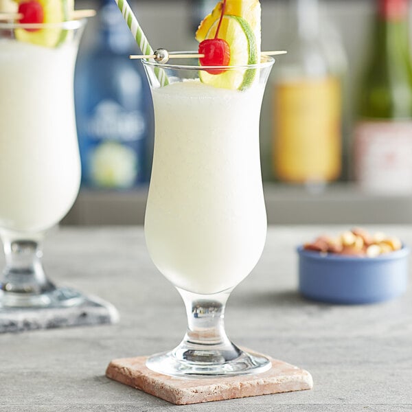 Two Pasabahce hurricane glasses filled with a white drink and pineapple garnish.