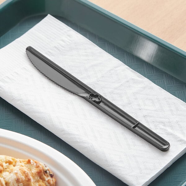 A black WeGo polystyrene knife on a napkin next to a white plate of food.