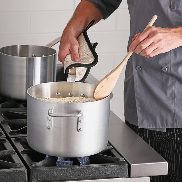 A person cooking food in a large silver Choice aluminum sauce pan on a stove.