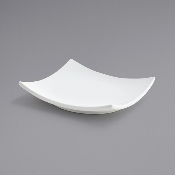 A Front of the House bright white square porcelain plate with a curved edge on a gray surface.