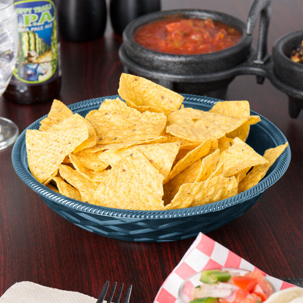 A blue polyethylene round weave basket filled with tortilla chips on a table in a Mexican restaurant.