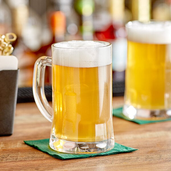 Two Acopa glass mugs of beer on a brown table.
